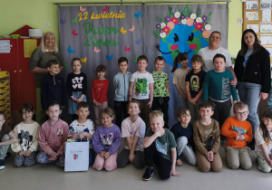Grupowe zdjęcie dzieci wraz z paniami z grupy "Motylków" na tle przygotowanej wcześniej dekoracji tematycznej.