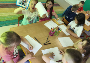 Kilkoro dzieci przy stole rysuje ilustrację do ulubionej bajki.
