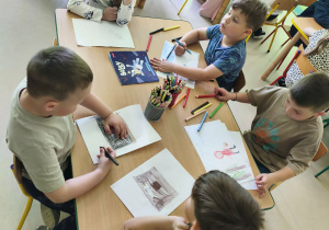 Kilkoro dzieci przy stole rysuje ilustrację do ulubionej bajki.