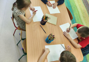 Kilkoro dzieci przy stole rysuje ilustrację do ulubionej bajki.