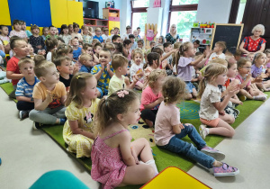 Przedszkolaki siedzą na dywanie i śpiewają piosenkę na powitanie.