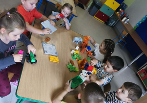 Chętne dzieci bawią się kolorowymi klockami przy stoliku.