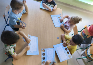 Dzieci przy stoliku tworzą pracę plastyczną "Mój wagonik".