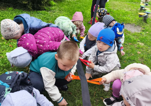Maluszki dotykają mokrą trawę w ogrodzie przedszkolnym.