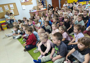 Przedszkolaki siedzą na dywanie i uważnie słuchają dźwięków płynących z akordeonu.