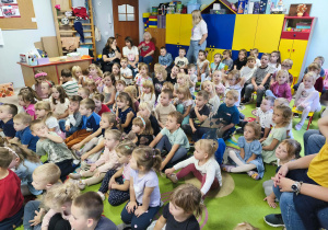 Przedszkolaki siedzą na dywanie i uważnie słuchają zagadek muzycznych z wykorzystaniem akordeonu.