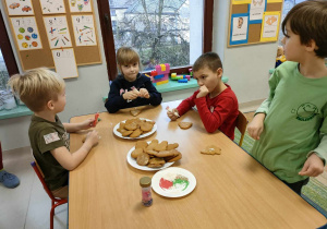 Kilkoro dzieci przy stole zaczyna zdobić wcześniej przygotowane pierniczki.