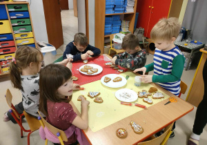 Kilkoro dzieci przy stole podczas ozdabiania pierników.