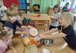Dzieci wrzucają pokrojone składniki do dużej miski.